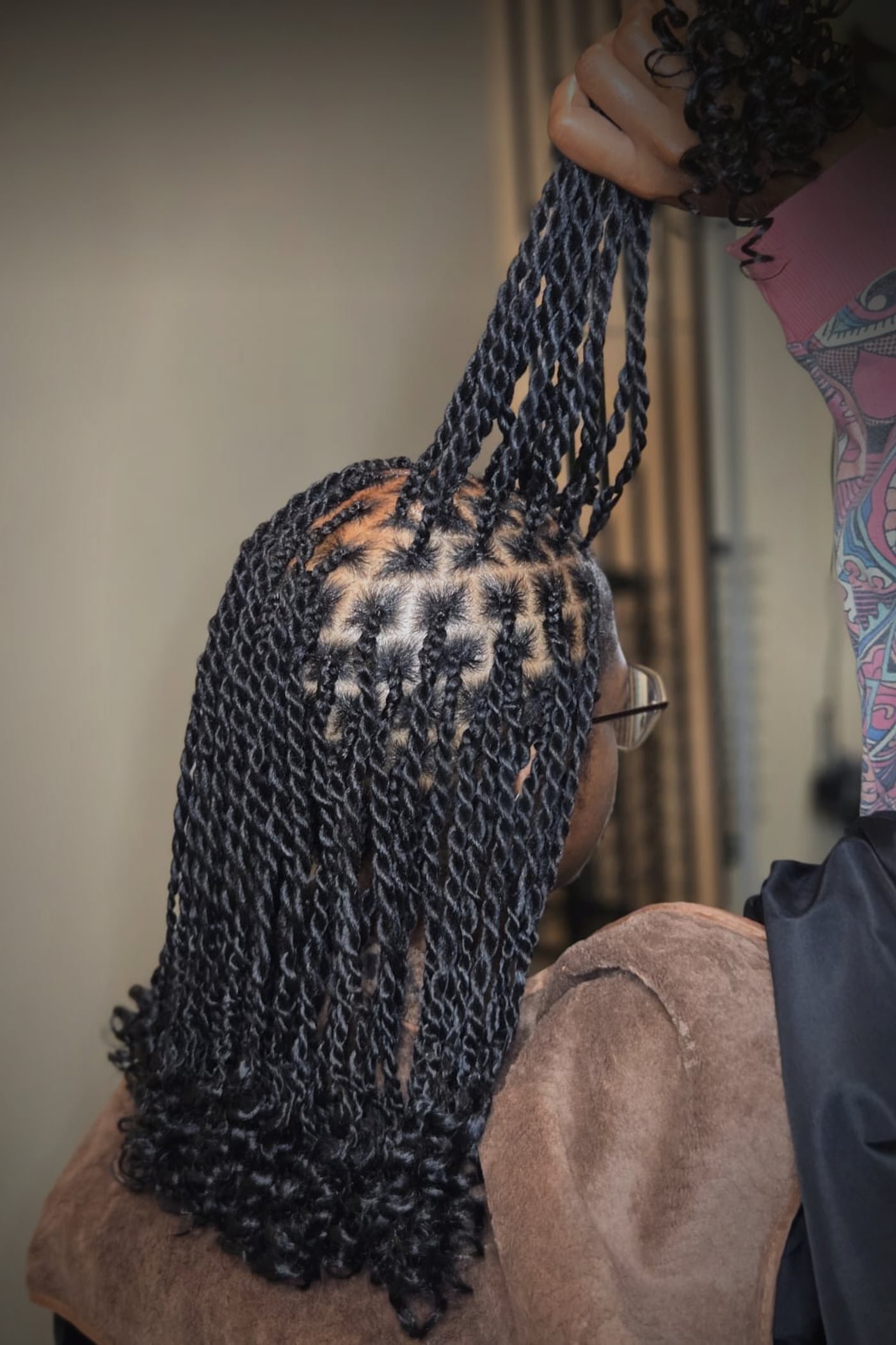 Golden-brown box braids with triangle parting, held mid-install by the braider's hand — real work from the Jemoel Lux Braids chair