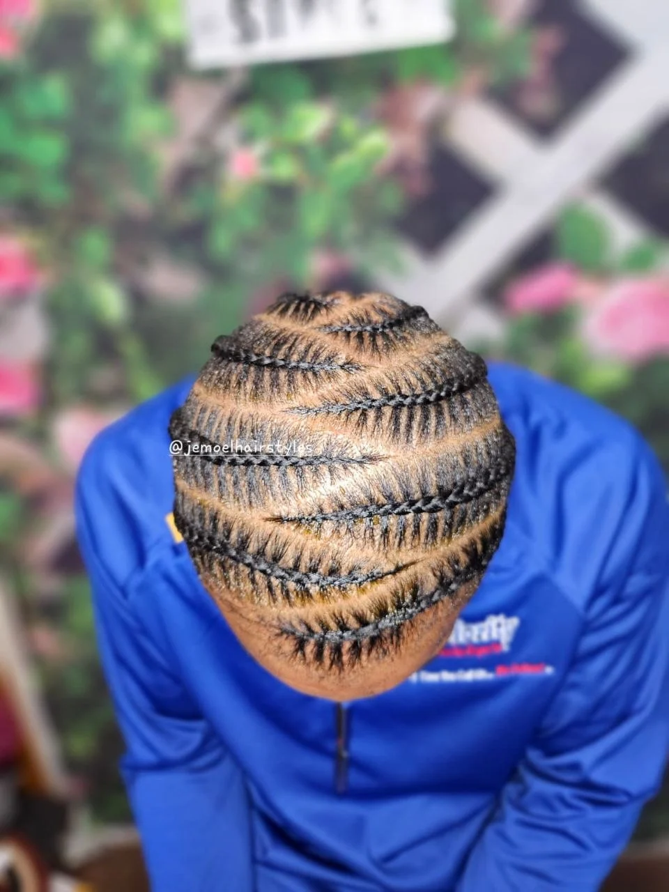 Overhead view of a man's head with tight stitch braids running from the front hairline to the back, wearing a blue jacket.