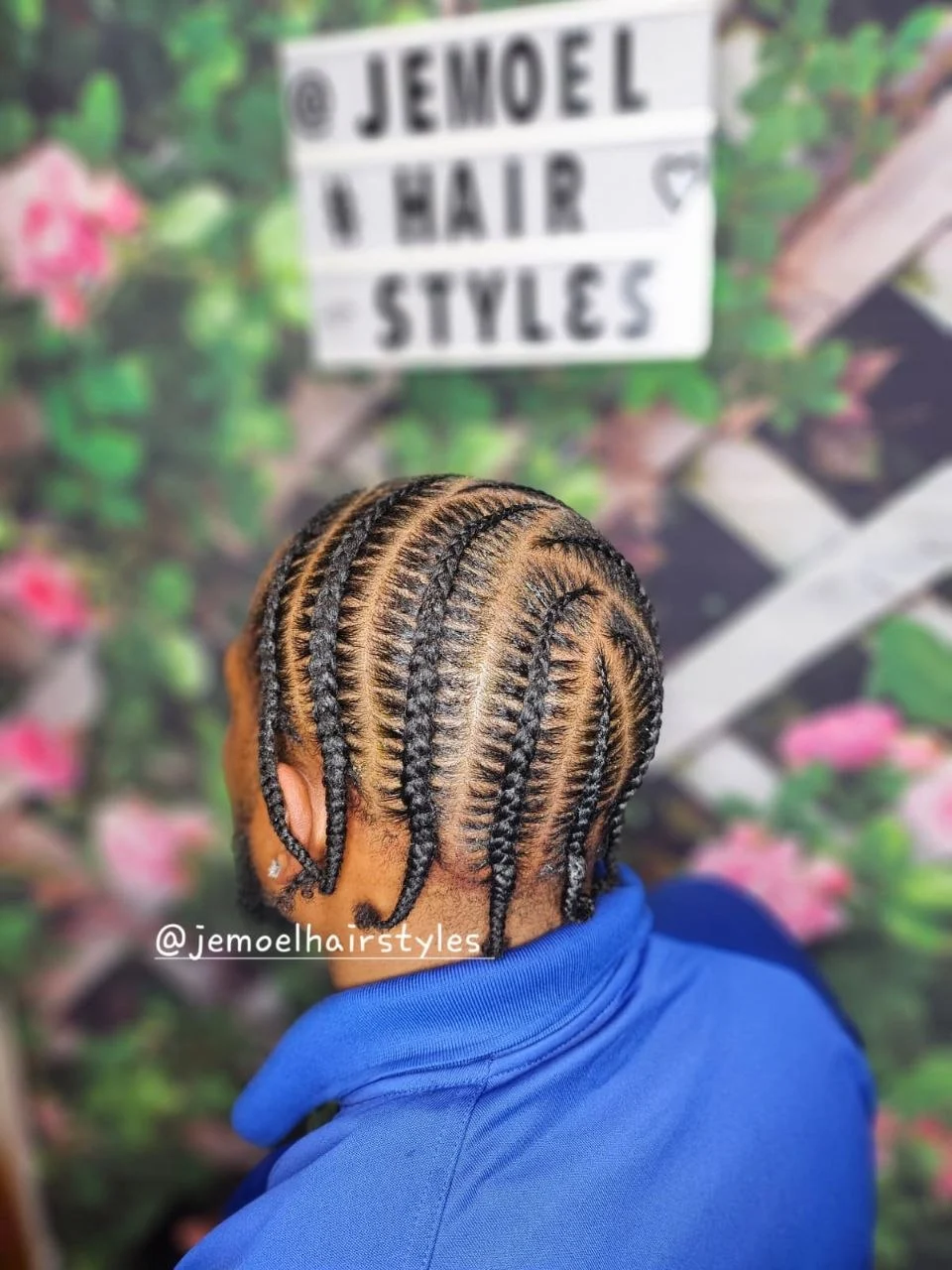 Back view of a man's head showing neat stitch cornrow braids, wearing a blue jacket.