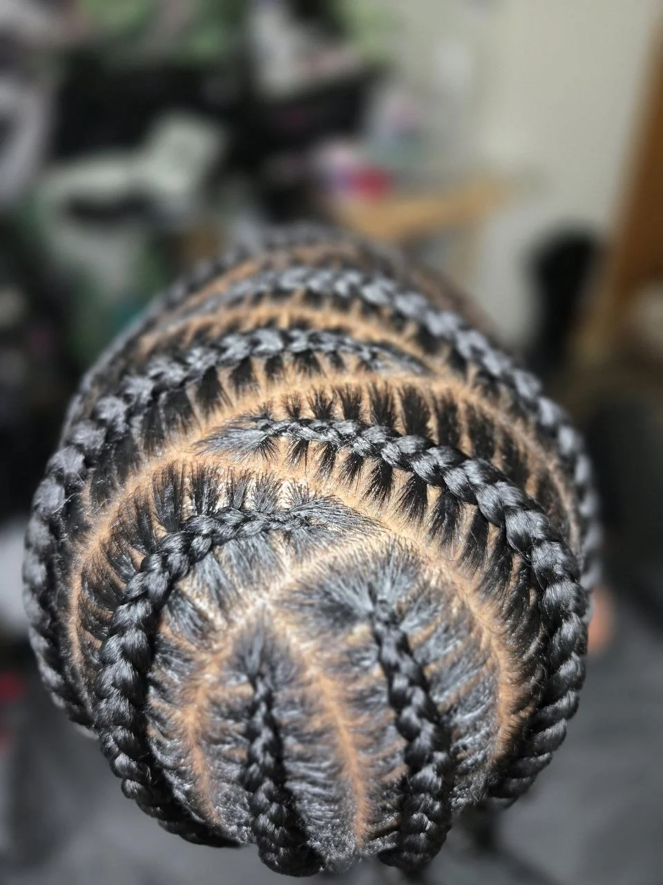 Top-down close-up of a man's scalp with a neat stitch braid cornrow pattern.